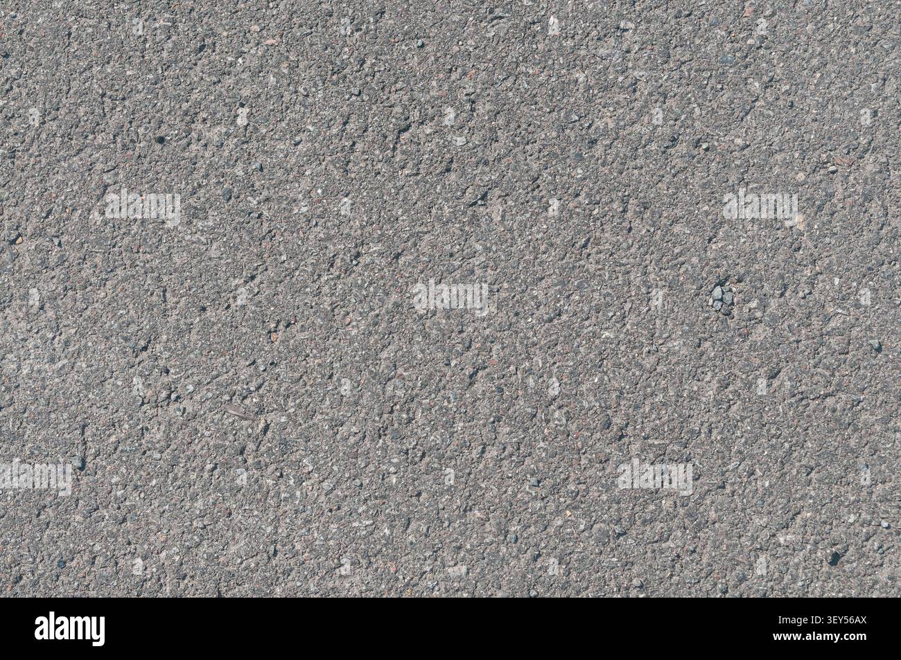 A close-up view of a gray asphalt road surface showing detailed texture, small pebbles, and coarse grain. Ideal for background or construction themes. Stock Photo