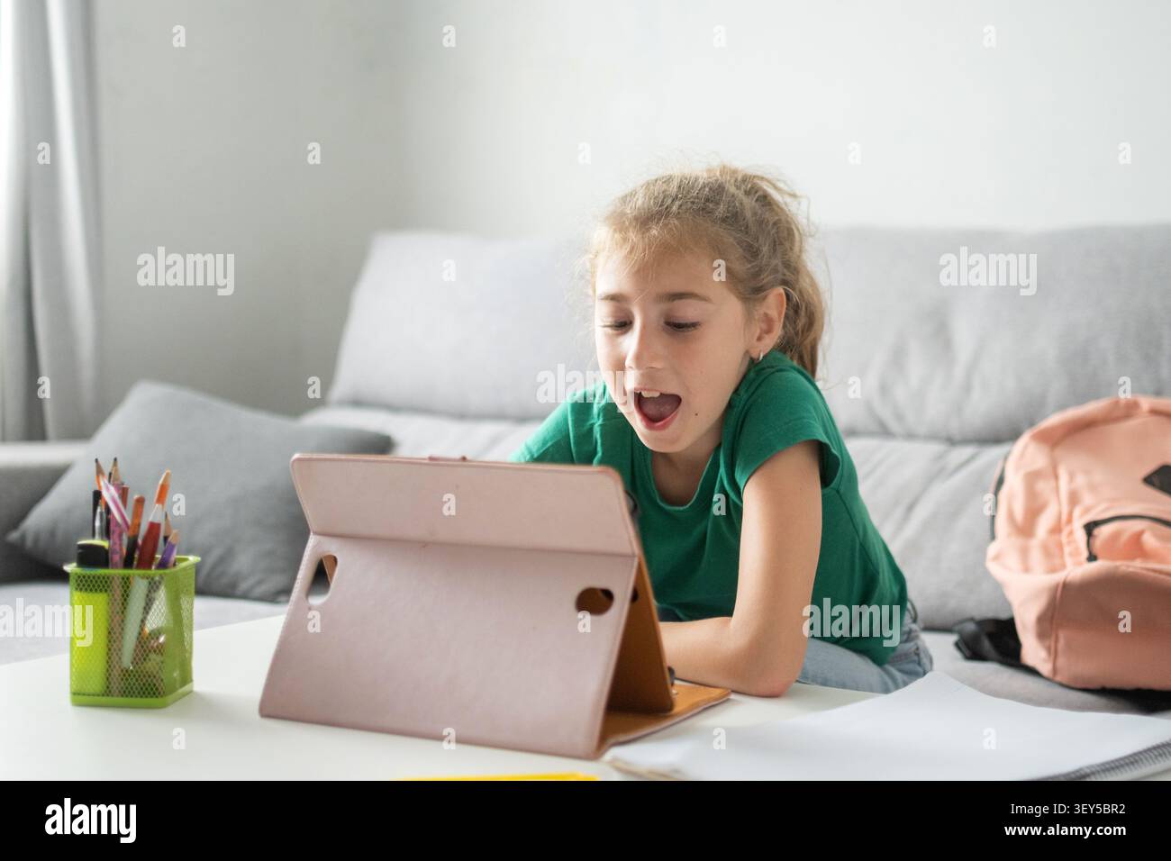 Happy elementary school girl using a digital tablet while studying at home. Stock Photo