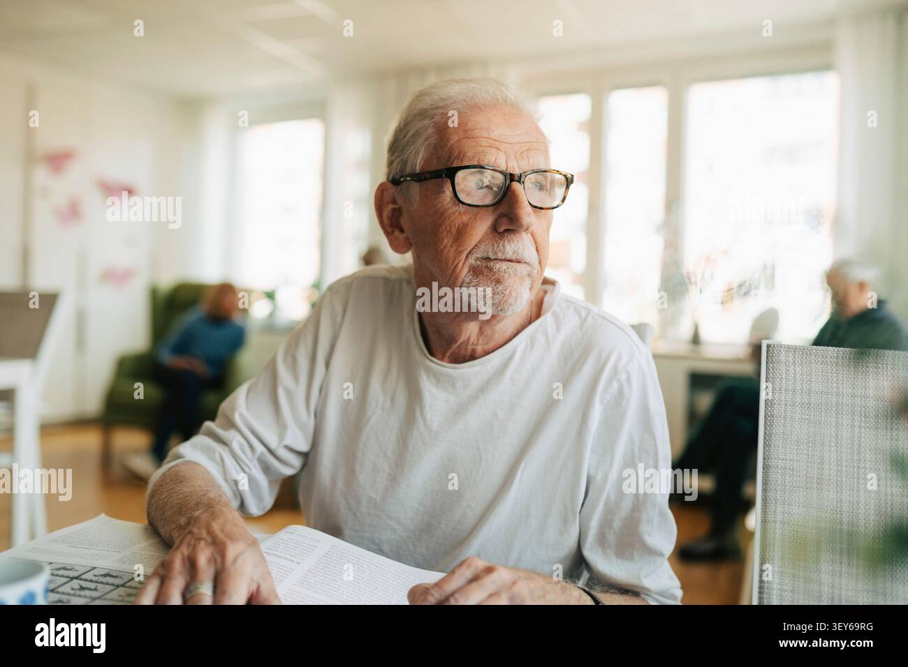 Thoughtful senior man looking away while sitting at table with book Stock Photo