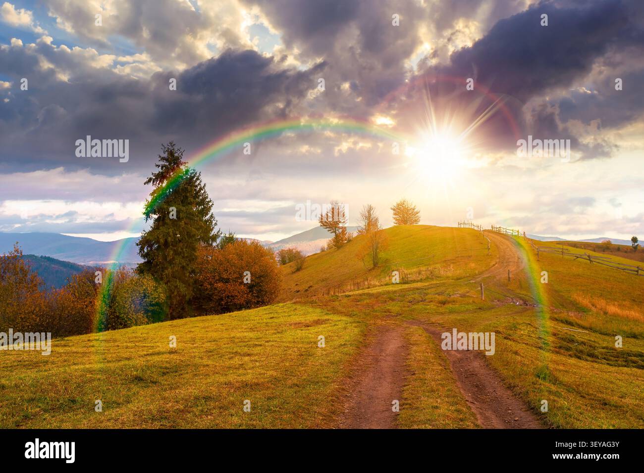 sunset over winding rural dirt path through hill. rolling countryside of ukraine in fall color. cloudy sky in evening light. carpathian mountains in a Stock Photo