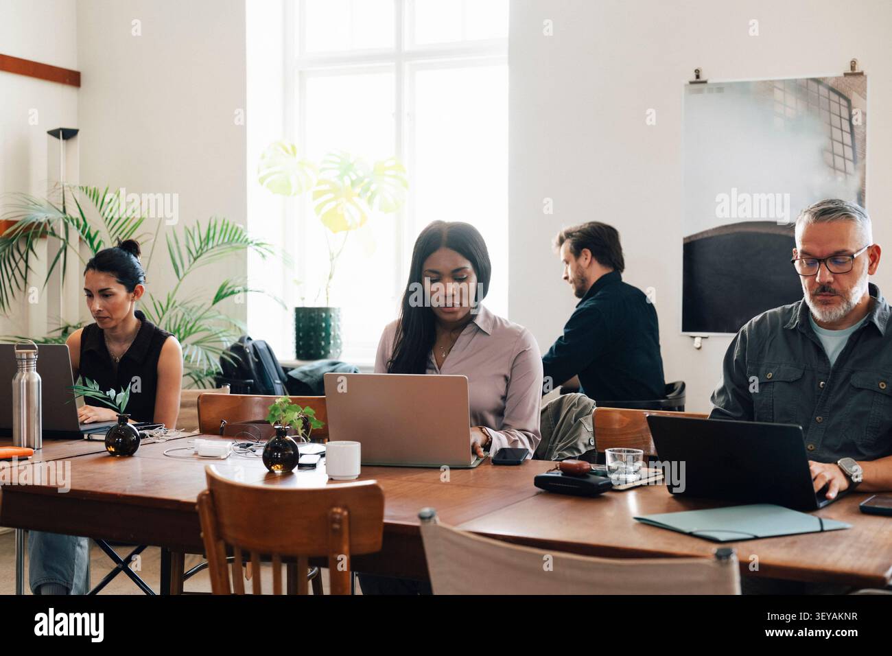 Diverse freelancers managing their tasks on laptops while working at shared open-plan workspace table Stock Photo