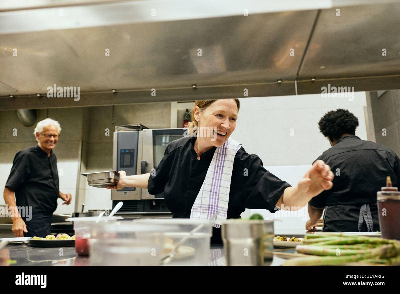Group of happy chefs communicating with each other while working in busy restaurant kitchen Stock Photo