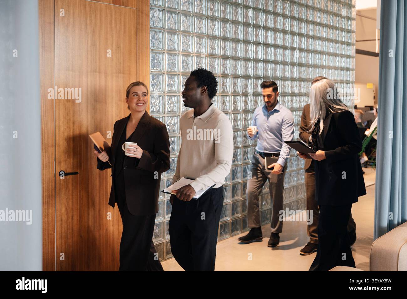 Group of diverse business colleagues walking and talking in office hallway Stock Photo