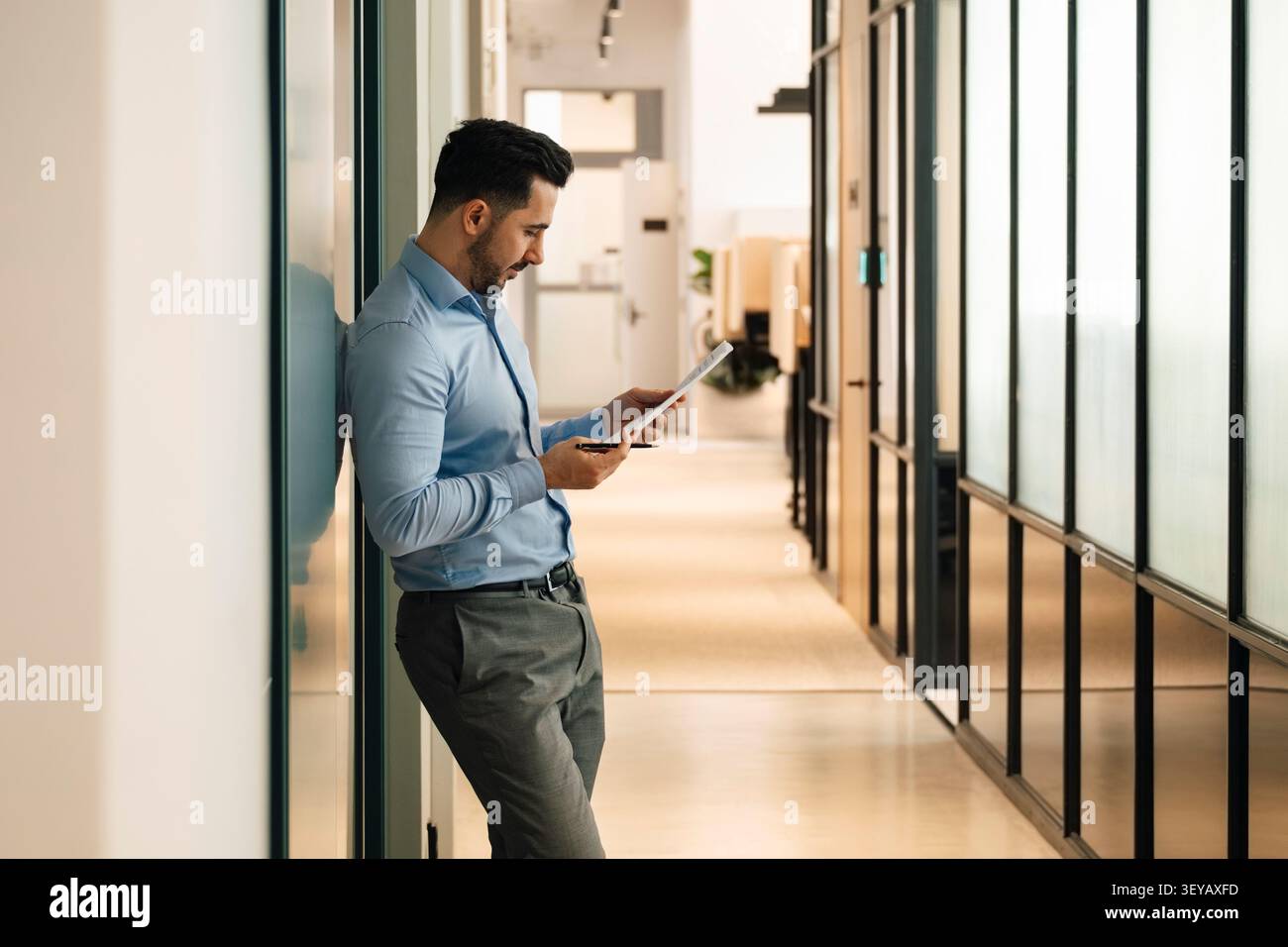 Businessman analyzing reports while leaning on wall in office hallway Stock Photo