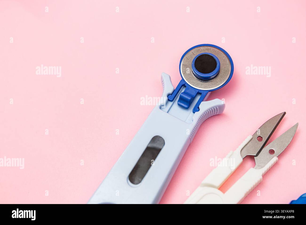 Minimal flat lay featuring a rotary cutter and thread snips on a soft pink background with ample copy space for creative projects, tailoring essential Stock Photo