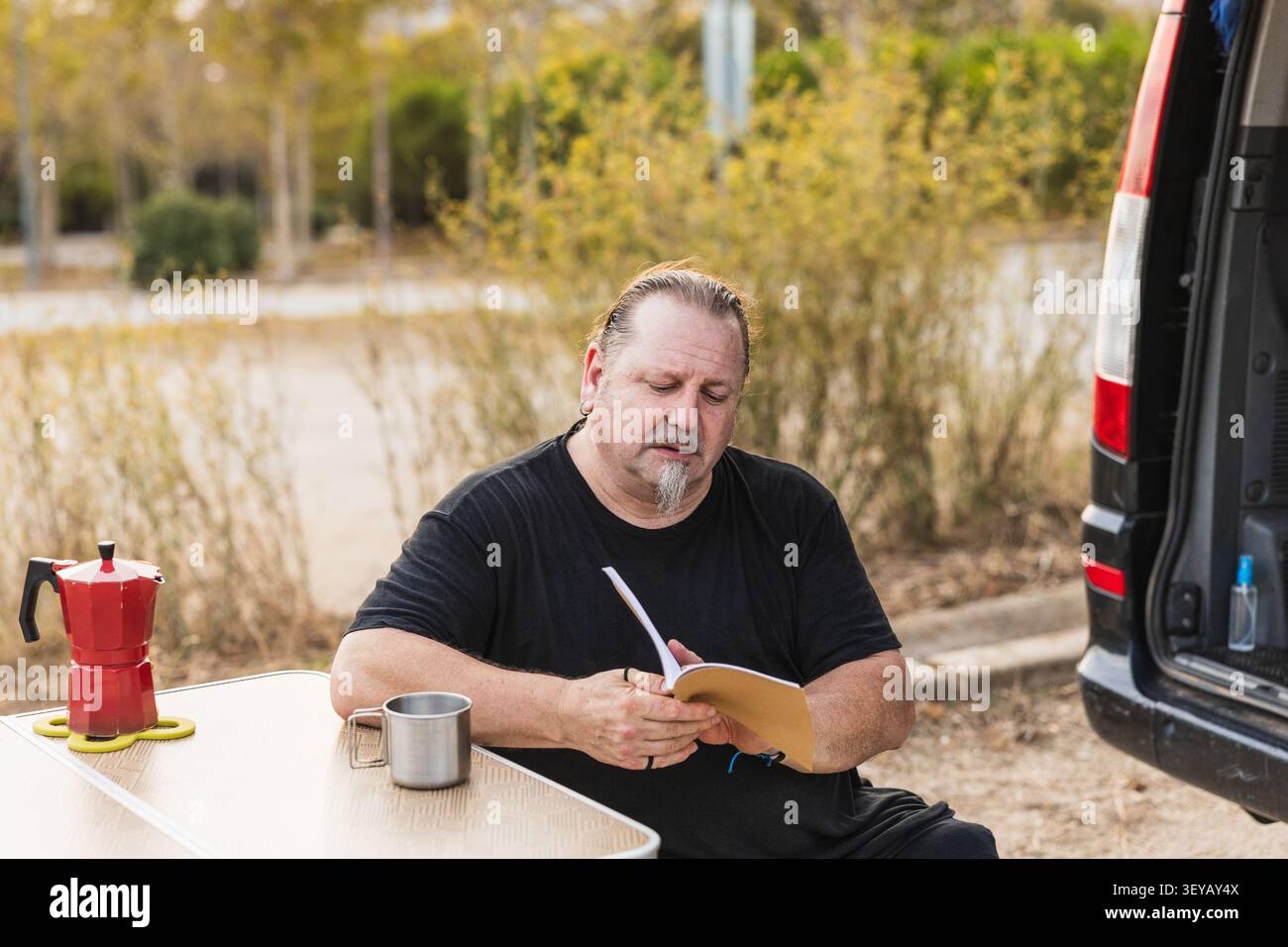 Mature man reading book while camping with van Stock Photo