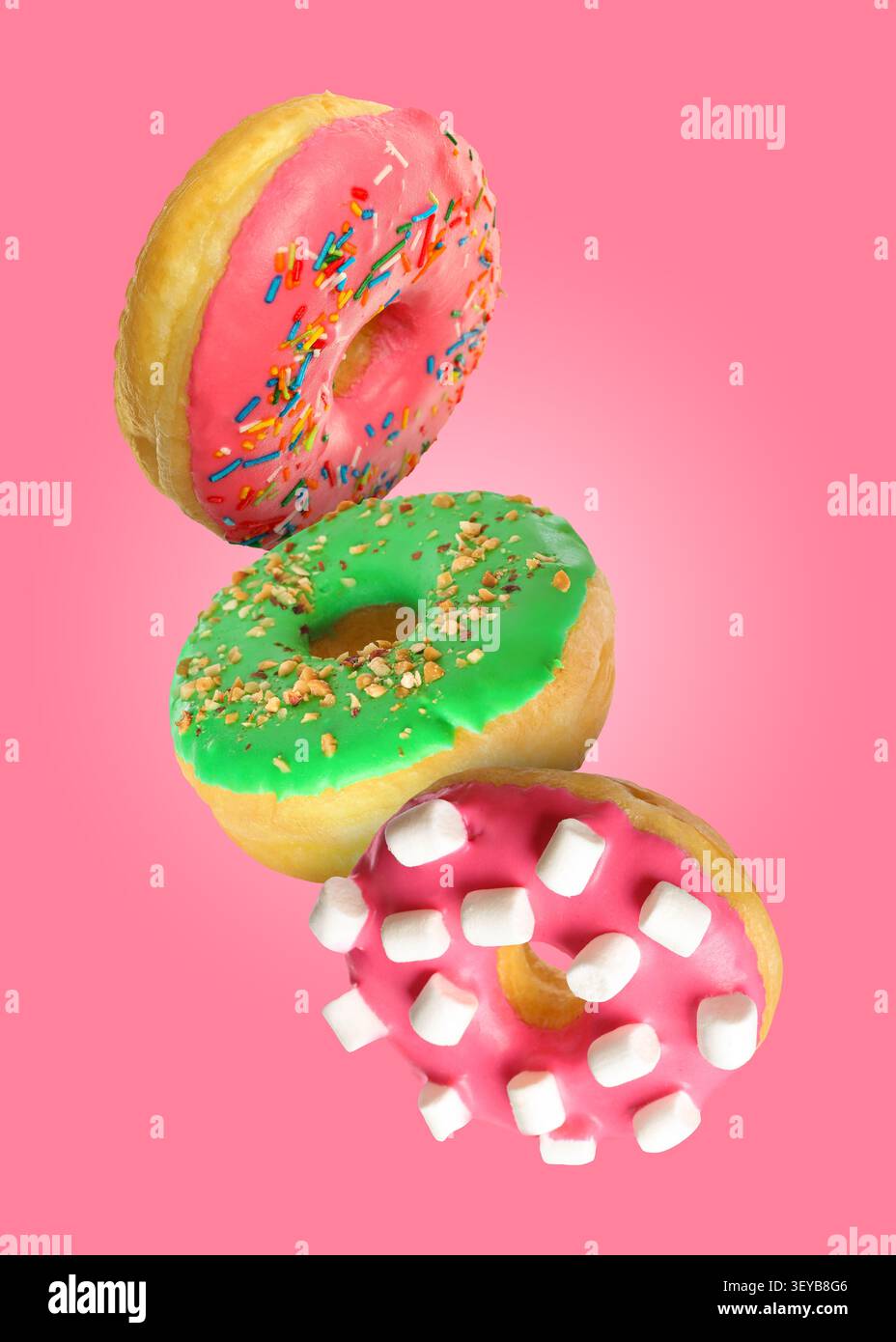 Tasty donuts covered with icing falling on pink background Stock Photo
