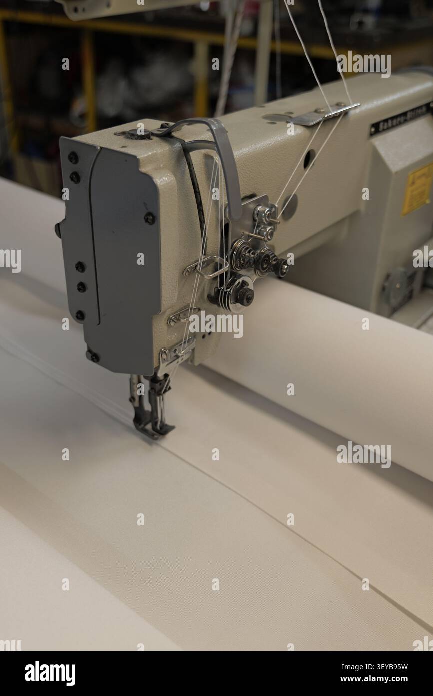 Industrial sewing machine performing a close up stitch on a white fabric curtain in a textile factory, creating durable seams for various manufacturin Stock Photo