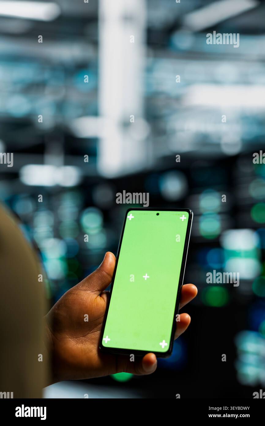 Data center programmer works with a chroma key smartphone, using an editable screen to review performance data. Stock Photo