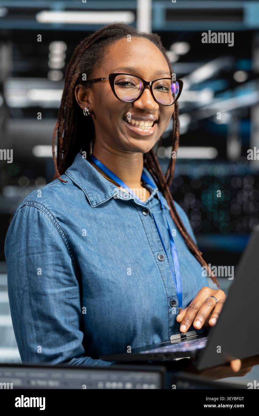 Friendly IT technician in data infrastructure center tracking system operational performance. Stock Photo