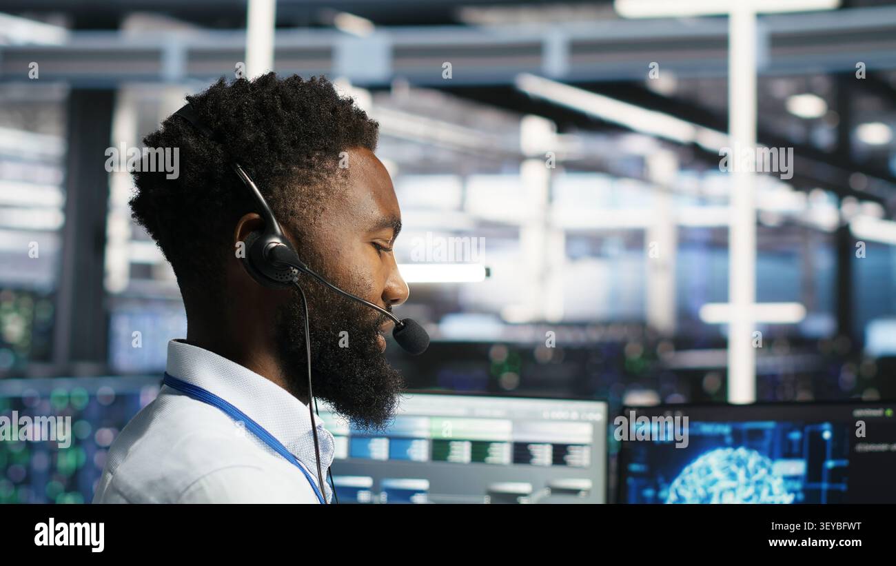 Server room employee talking in headset mic, coordinating technicians setting up hardware for AI deployment. Stock Photo