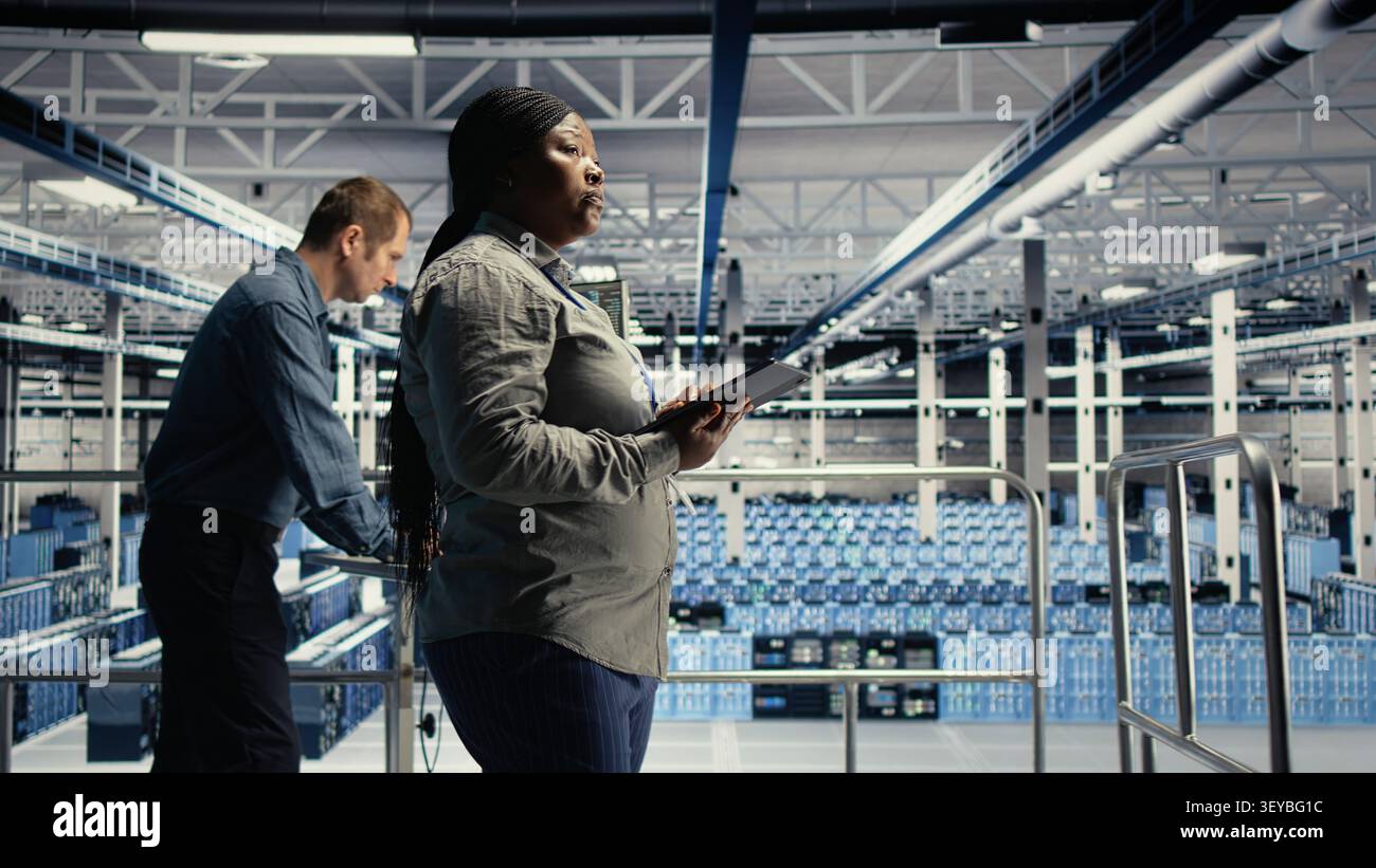 IT expert checks server environment activity working with digital tablet while walking on industrial platform. Stock Photo