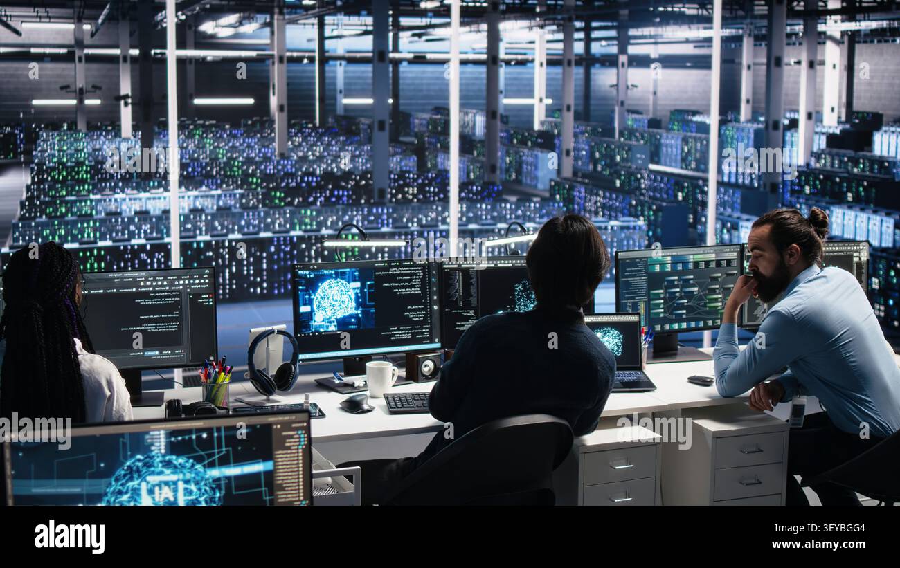 Server room system administrators working with AI to check digital infrastructure diagnostics with IT professionals in server facility assessing operational performance data using AI tools. Stock Photo