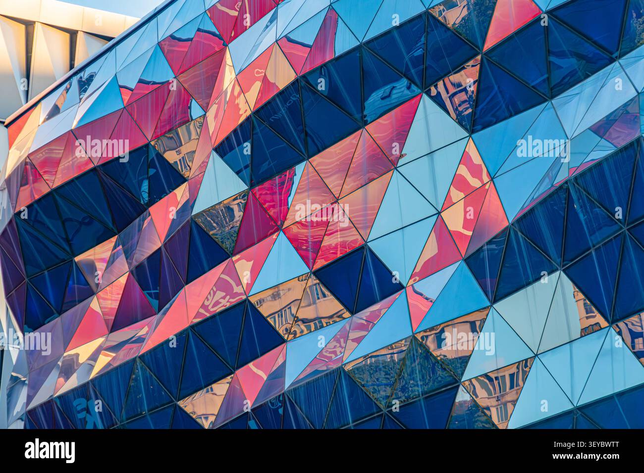 Striking architectural facade composed of triangular panels, reflecting vibrant colors and urban environment, showcasing dynamic geometric patterns wi Stock Photo