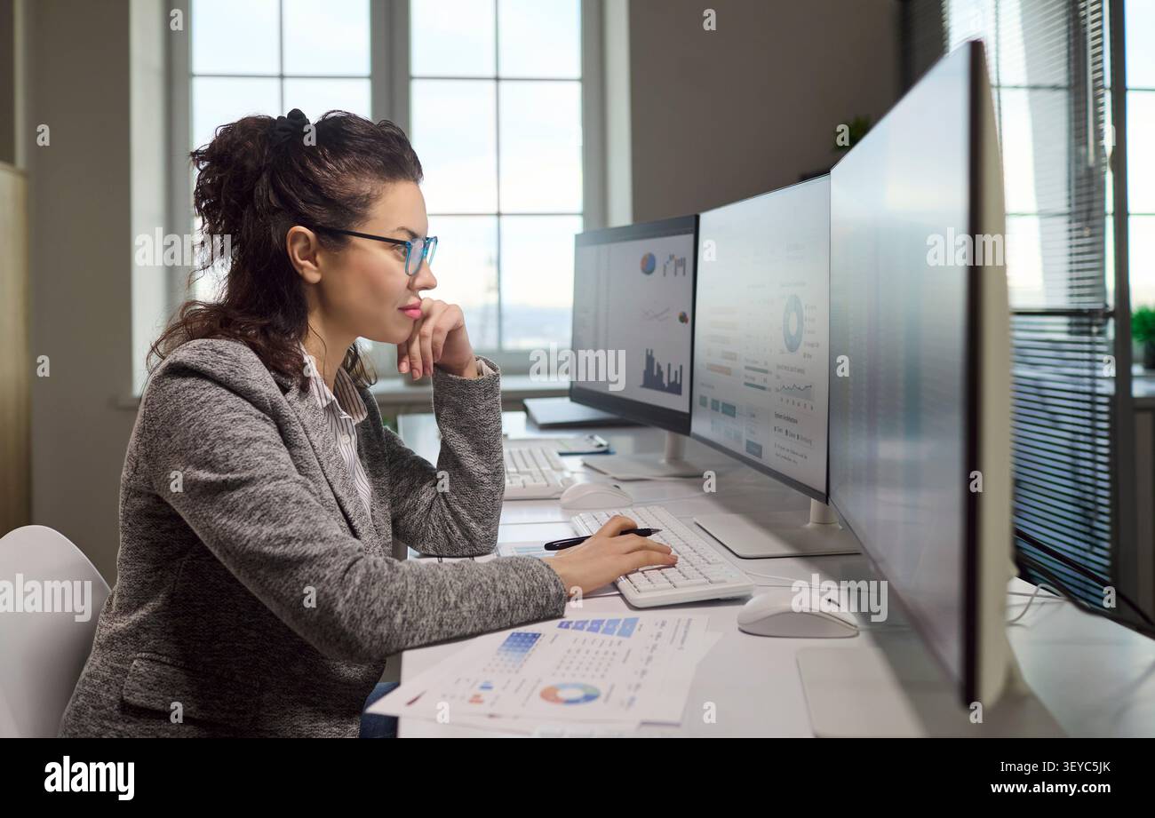 Female accountant analyzing financial data on computer monitors with spreadsheets Stock Photo