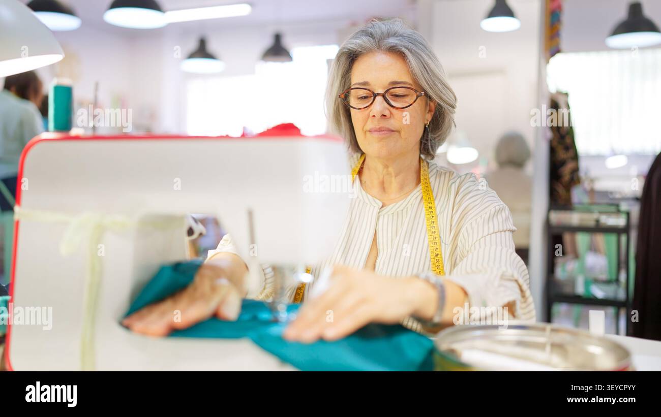 Mature woman sewing fabric in creative workshop Stock Photo