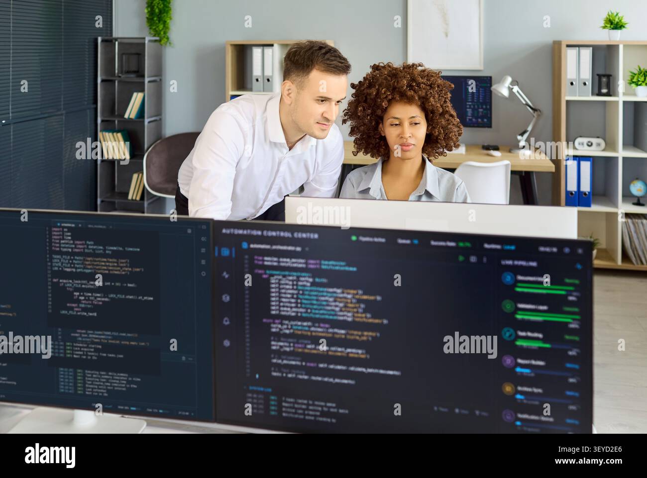 Developers pair programming and reviewing code on monitors in modern office Stock Photo