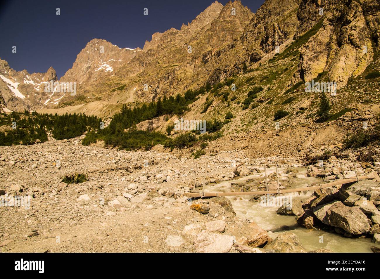 Mountain stream flows through rocky landscape with small bridge and Stock Photo