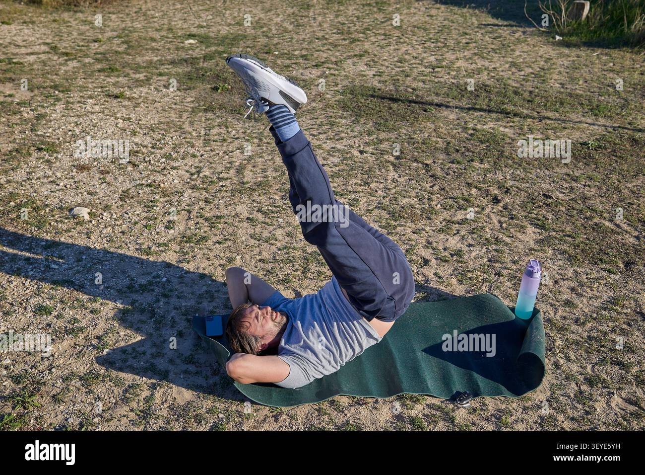 A man performing a vertical leg raise while lying on a fitness mat during an outdoor workout session. Stock Photo