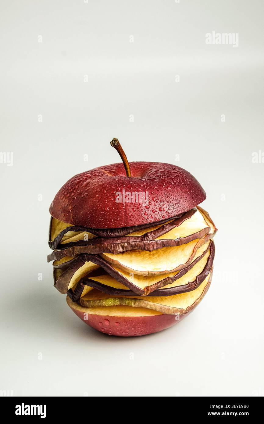 Deconstructed red apple with layered dried slices and water droplets on clean white background Stock Photo