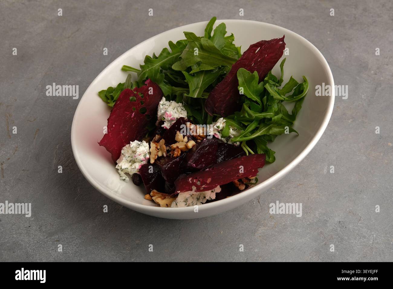 Fresh beet salad with arugula, goat cheese and walnuts in white bowl on stone surface Stock Photo