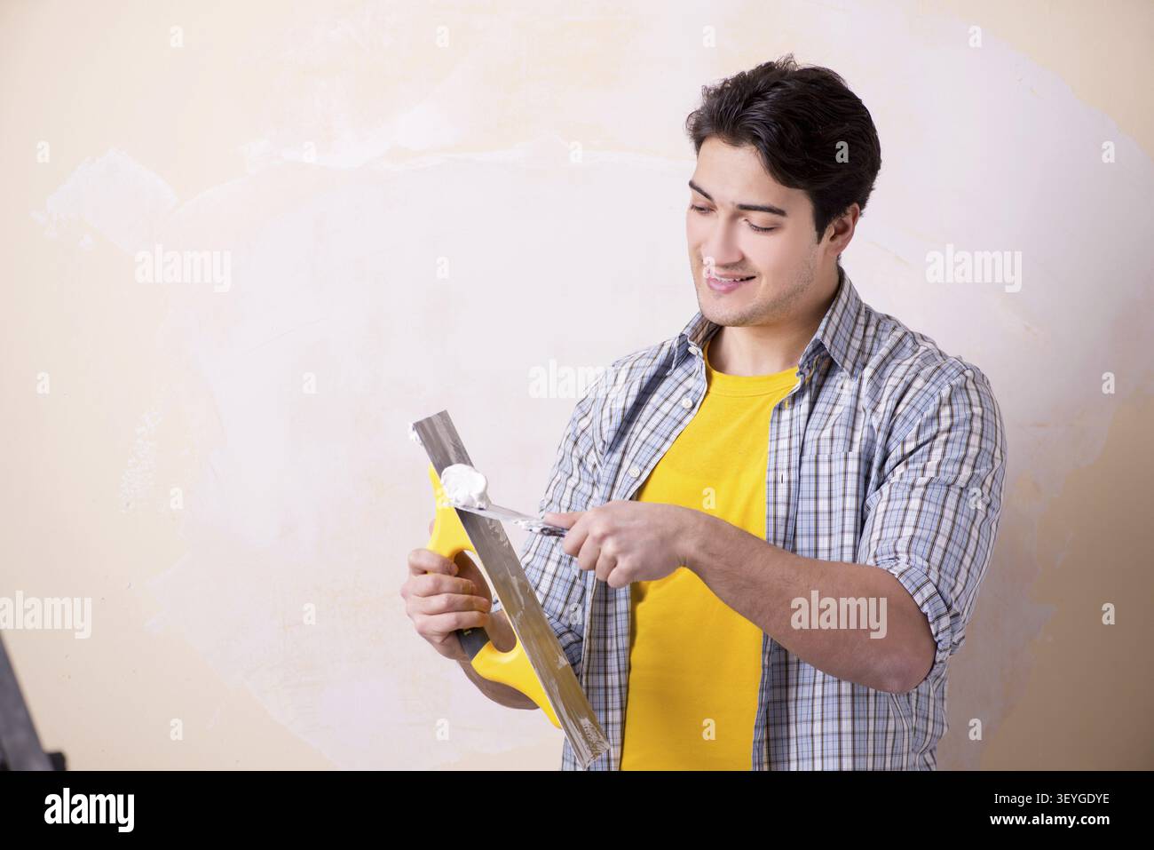 Young man applying plaster on wall at home Stock Photo