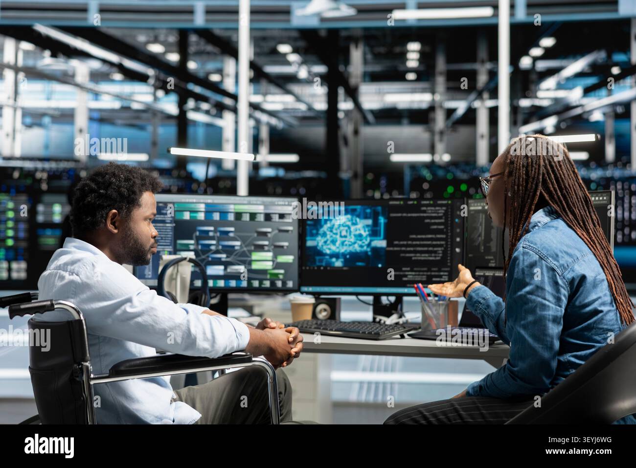 Worker using a wheelchair in a data center uses a computer to manage machine learning workloads, working with AI technology and high performance systems. Stock Photo
