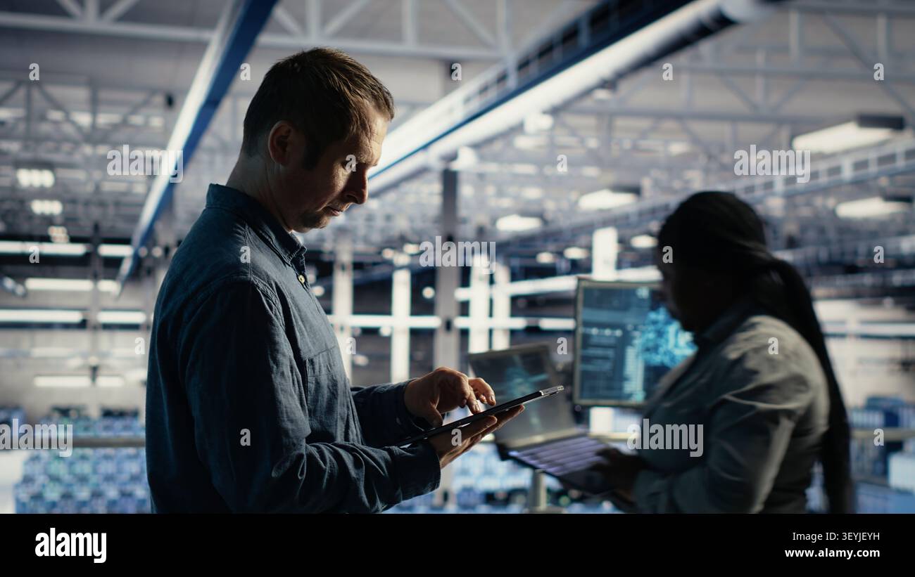 Data center technician monitors operational metrics on tablet inside a server room to improve infrastructure performance. Stock Photo