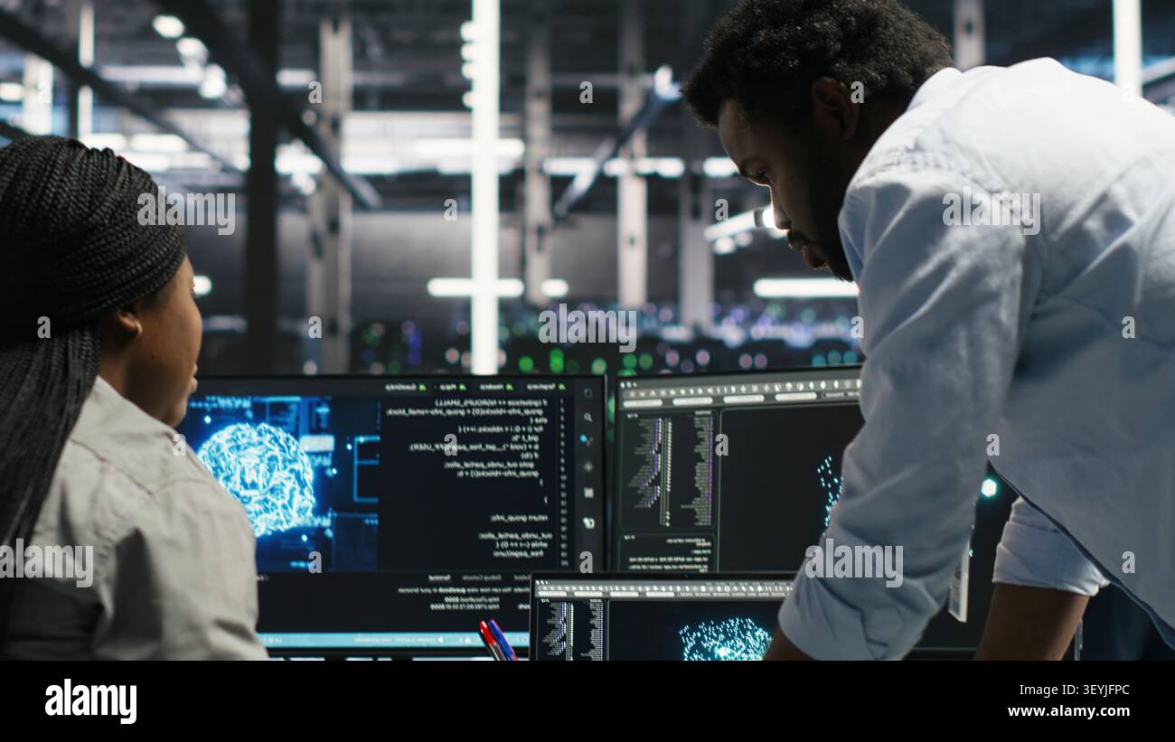 Server facility engineering team works with AI ML models to set up equipment. Teamworking colleagues work on AI programming tools in server environment, optimizing system. Stock Photo