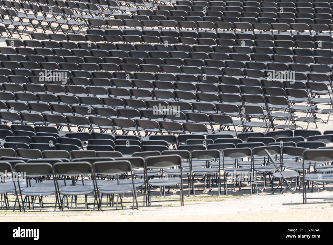 Hundreds of empty folding chairs are arranged in neat rows for a large outdoor event. The repeating pattern emphasizes scale and organization. Stock Photo