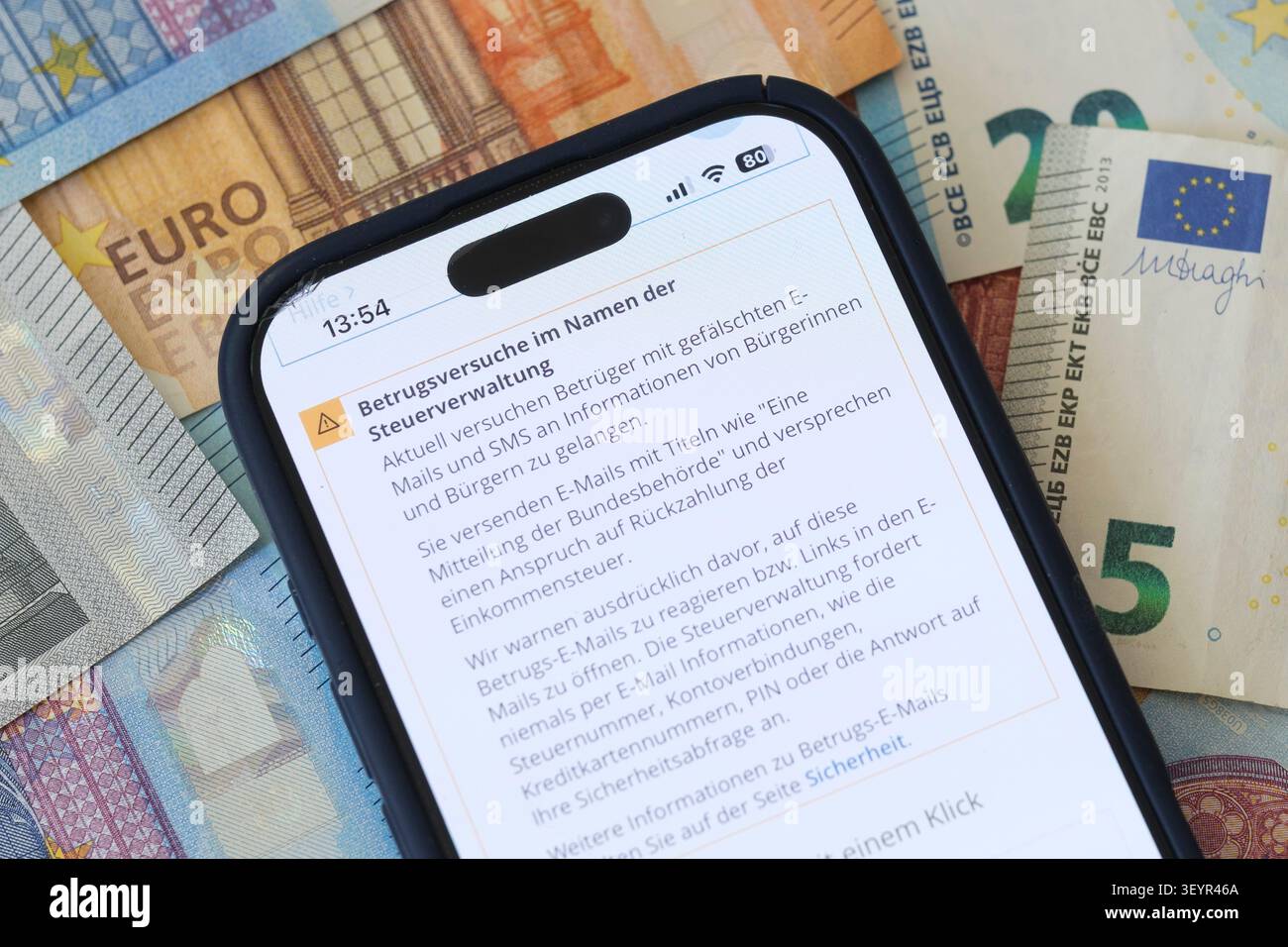A smartphone on a background of Euro banknotes displays an official warning regarding fraudulent scam attempts issued the tax administration Stock Photo
