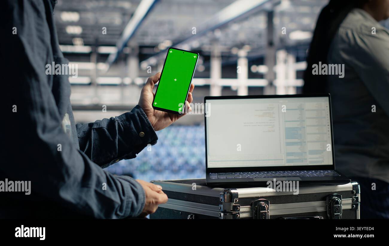 Software developer uses a green screen smartphone in a server room while waiting for code updates to finish. Stock Photo