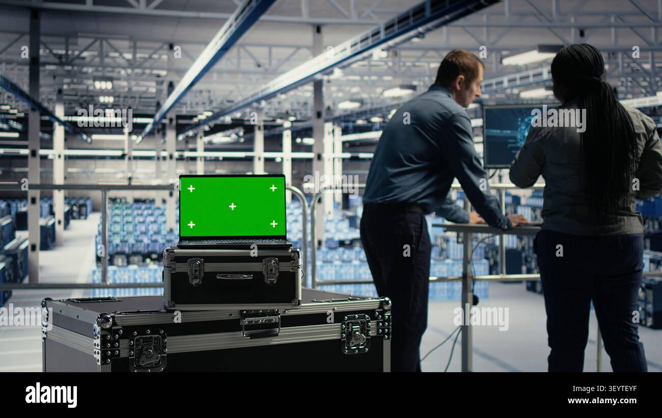 Programmers use green screen laptop in a data center to upgrade server hardware and improve workload capacity. Stock Photo