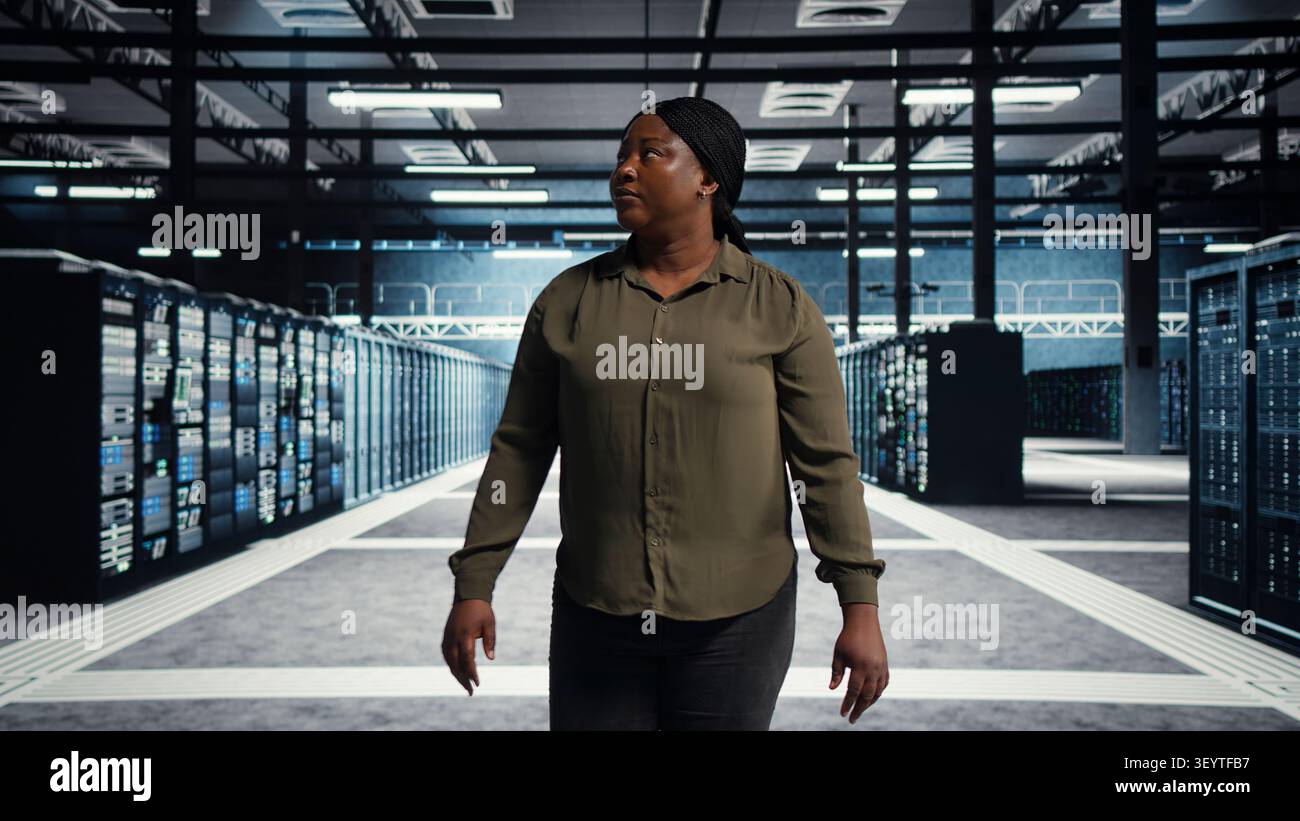 Software engineer walking in server facility, checking hardware for system stability. IT administrator supervising server environment room, checking infrastructure systems. Stock Photo