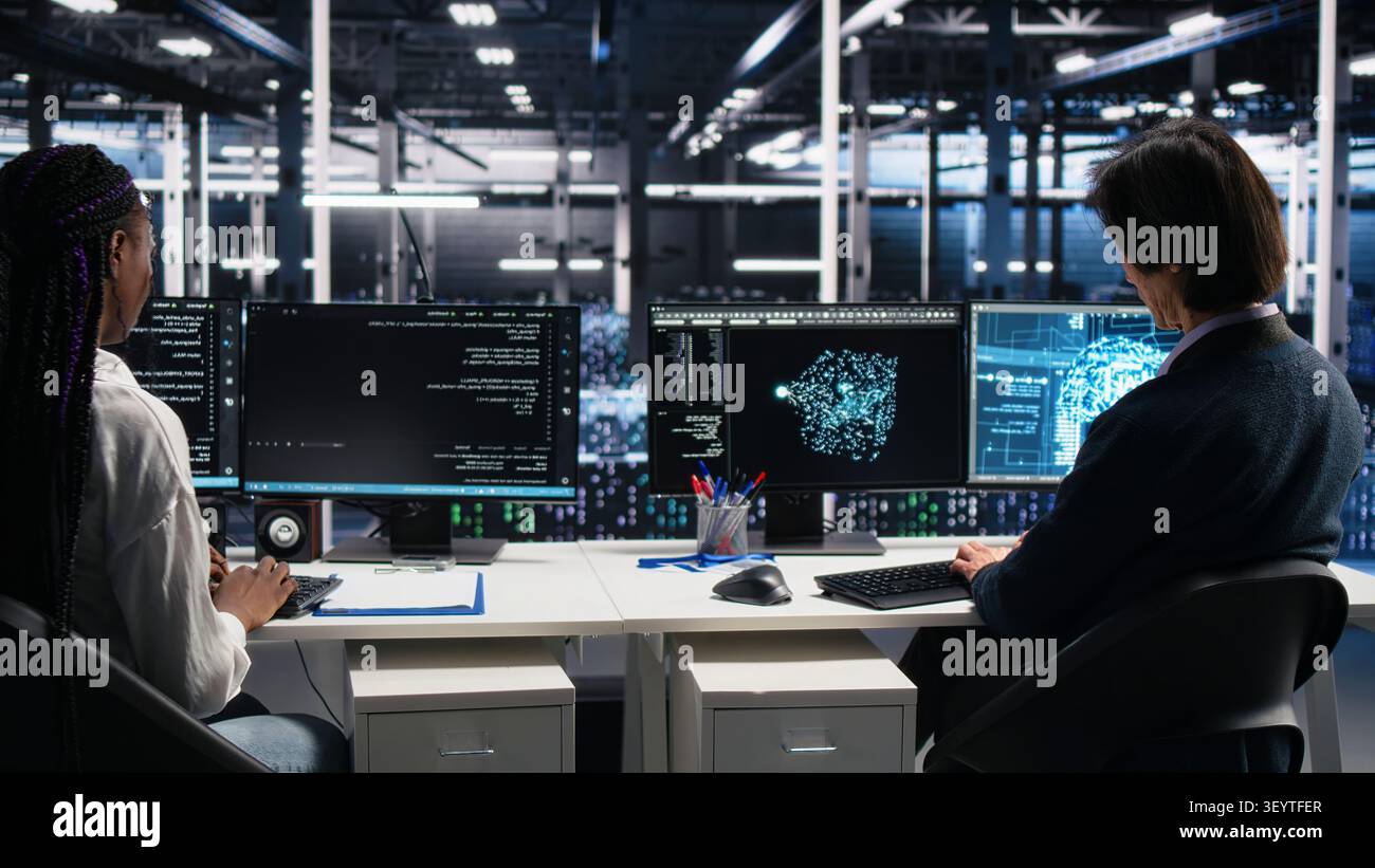 Server room system administrators working with machine learning models on computer to review data sets. Stock Photo