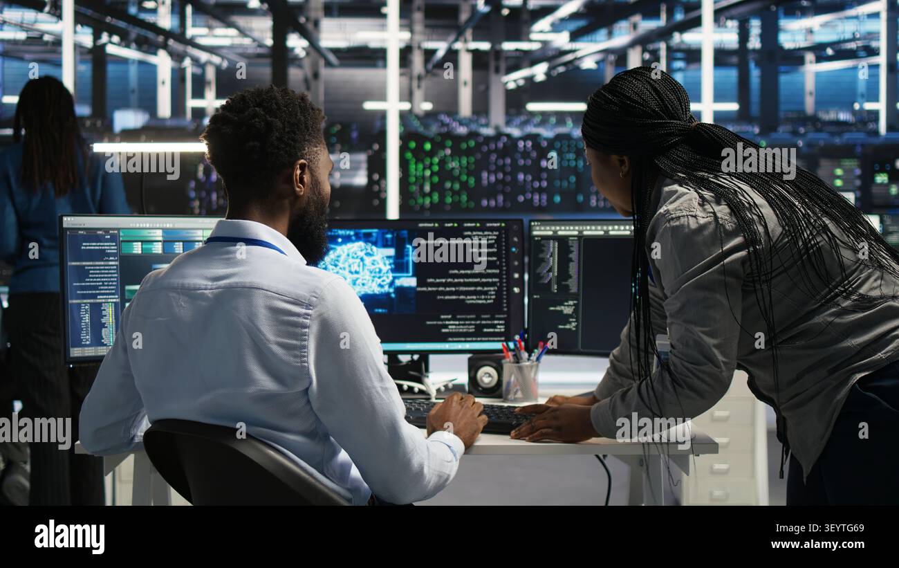 Server room supervisor overseeing work done by engineer working with deep learning models to review data sets. Stock Photo