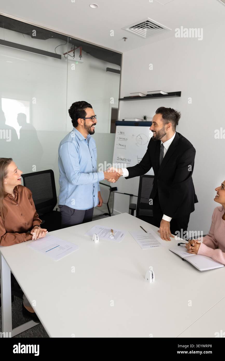 Two businessmen shake hands during group meeting in conference room Stock Photo