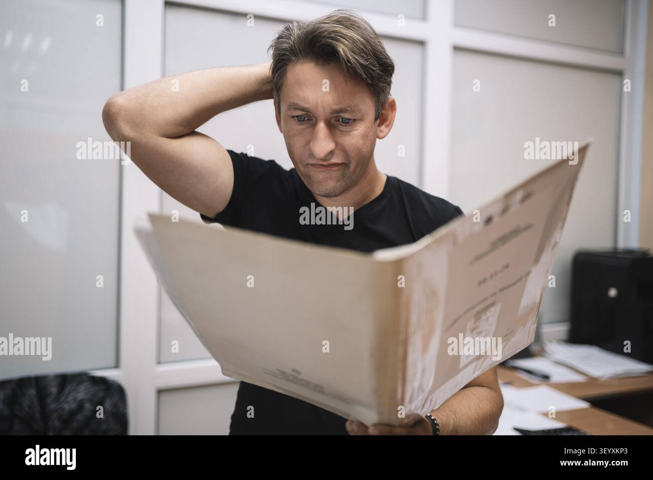 Concentrated worker studying paperwork. Man reading documents with puzzled expression in office. Stock Photo