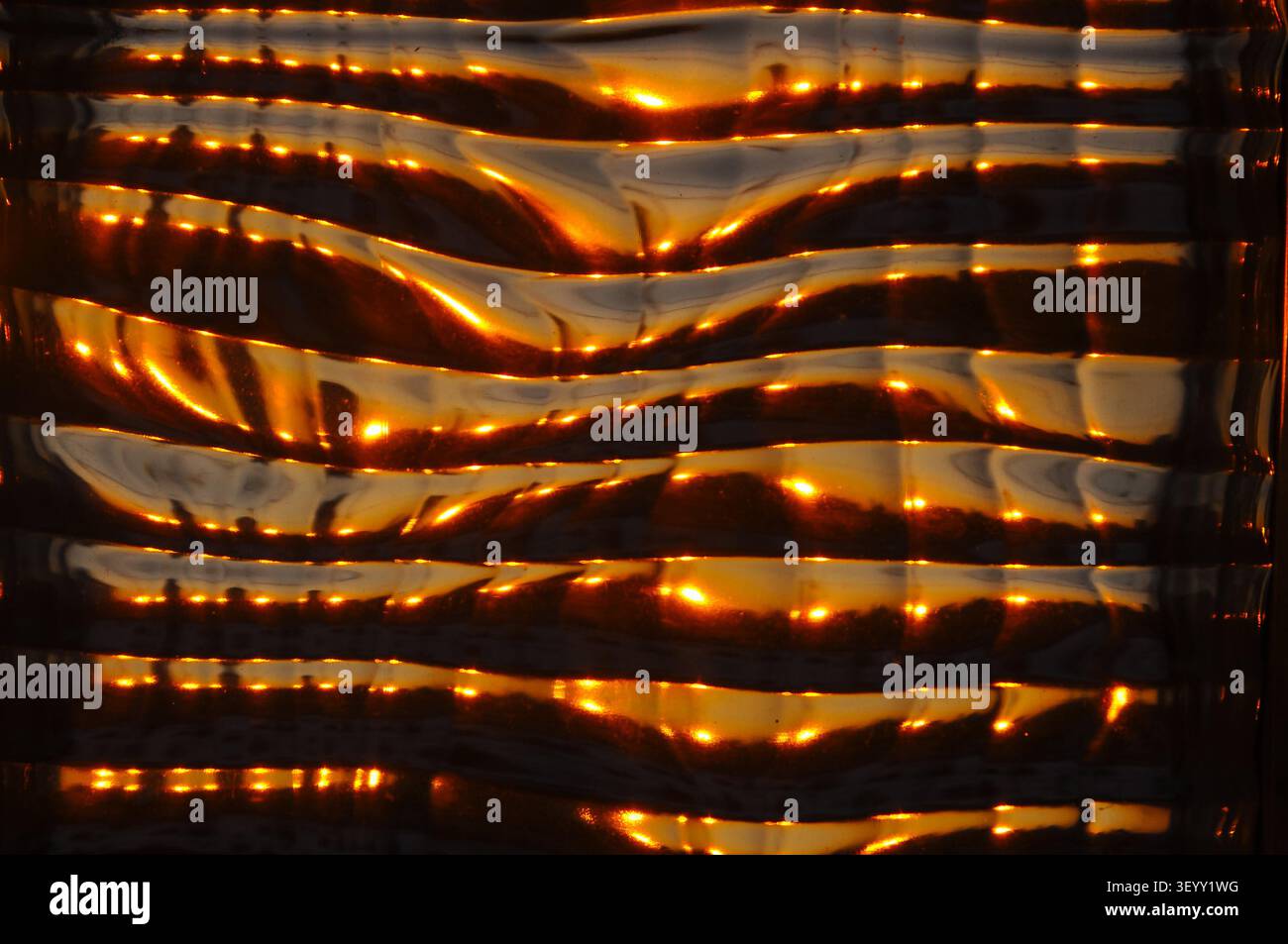 This image showcases a unique textured glass surface with warm, golden reflections, creating a captivating visual Stock Photo