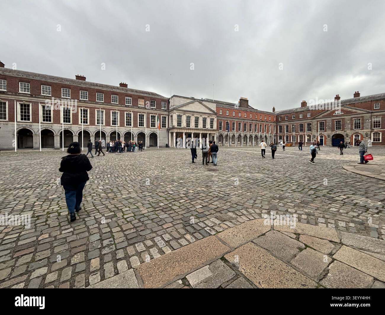 Tourists walking across the historic stone cobblestone courtyard of Dublin Castle under an overcast sky, Ireland - Smartphone Captured Stock Image