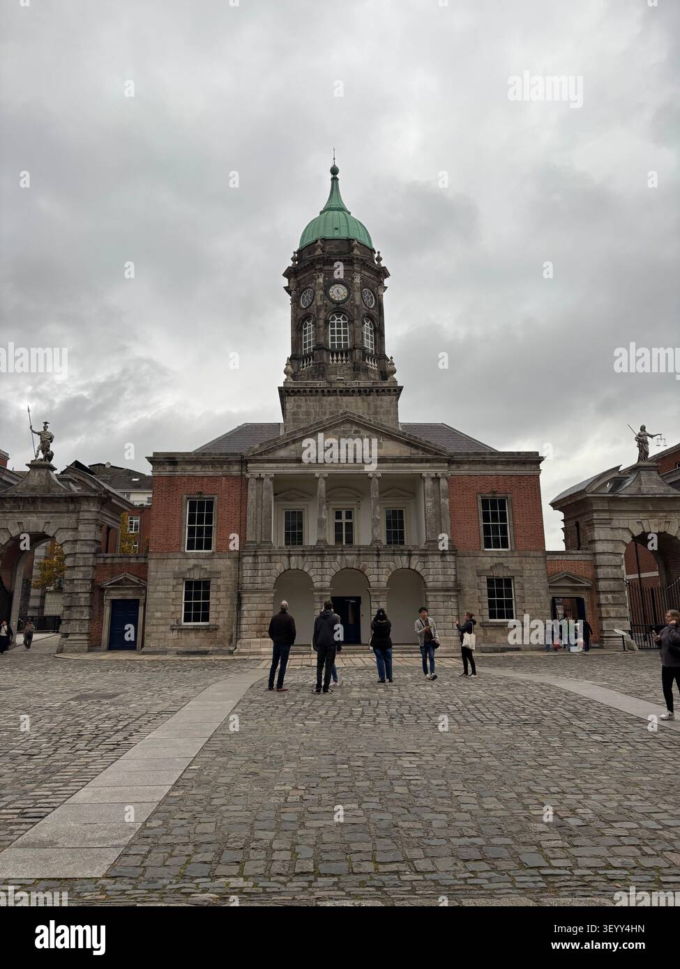 Tourists exploring the historic cobblestone courtyard of Dublin Castle in front of the prominent Bedford Hall tower, Ireland - Smartphone Captured Stock Image
