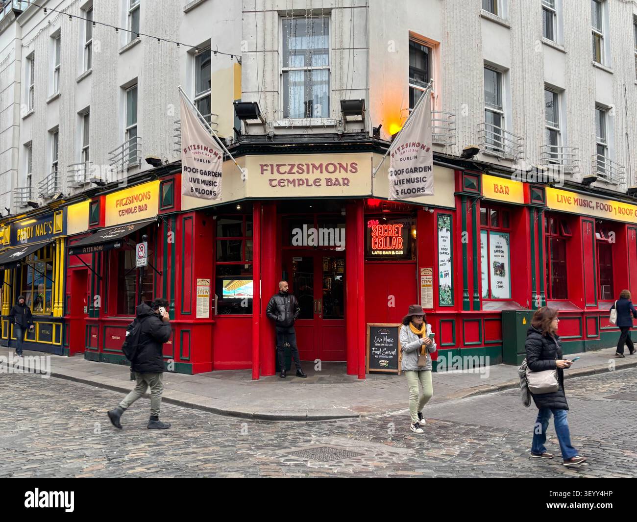 The vibrant red facade of Fitzsimons Temple Bar pub on a cobblestone street corner in the cultural quarter of Dublin, Ireland - Smartphone Captured Stock Image