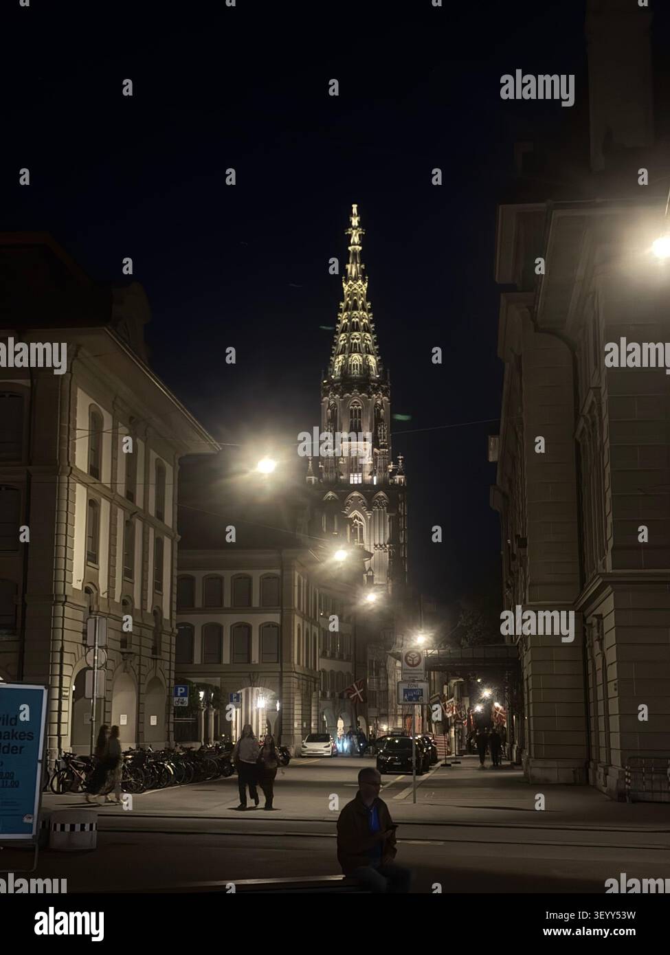City street scene at night looking towards the illuminated gothic spire of Bern Cathedral, Bern, Switzerland - Smartphone Captured Stock Image