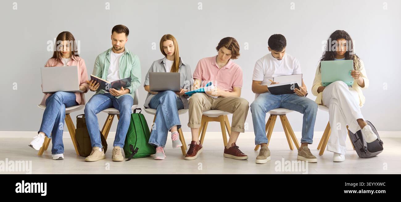 Diverse college students studying with laptops and notebooks against gray wall Stock Photo