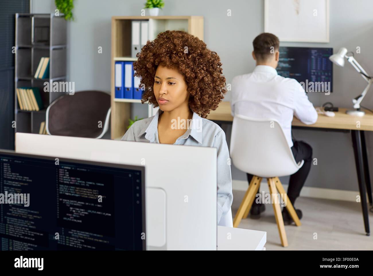 Female software developer coding at desktop in modern office workspace environment Stock Photo