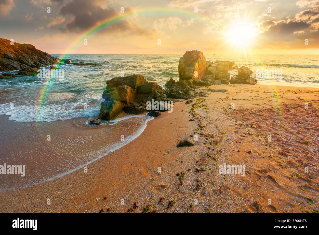 sunset over huge stones on the sandy beach. wonderful holiday season background at the sea. clouds on the blue sky above horizon. view of waves washin Stock Photo