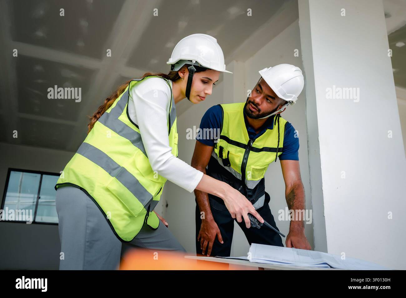 Construction Manager analyzing building blueprint indoor with Civil engineer while holding walkie talkie, scene for real estate property development a Stock Photo