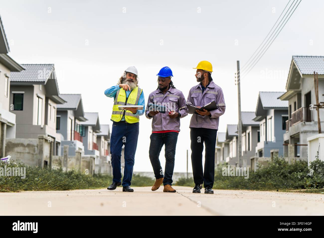 Construction engineers walking through residential development site to inspect and coordinate building progress, discussing work progress while walkin Stock Photo