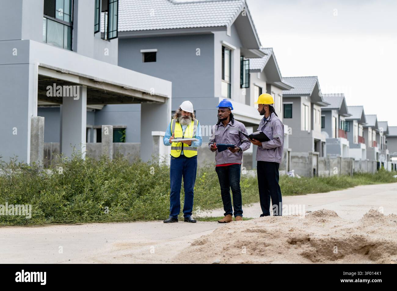 Construction engineers walking through residential development site to inspect and coordinate building progress, discussing work progress while walkin Stock Photo