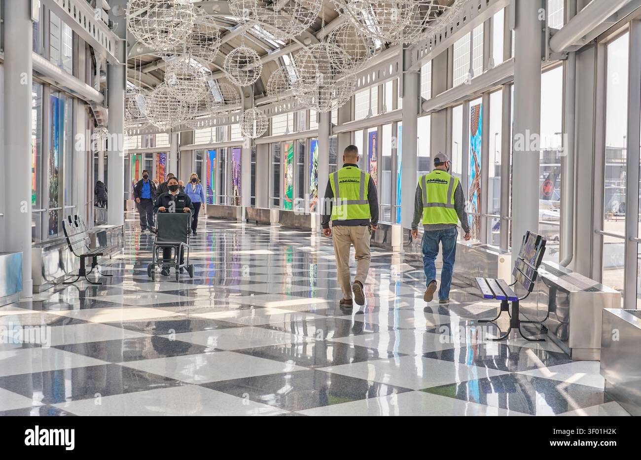 CHICAGO, IL, USA - MARCH 03, 2021: Workers in safety vests walk through a spacious and well-lit corridor at an airport. The passageway features large Stock Photo